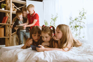 La fotografia mostra bambini e bambine che giocano con tablet e smartphone evidenziando come ormai anche i più piccoli usino sempre di più questi dispositivi, mettendo a riscio la loro salute.